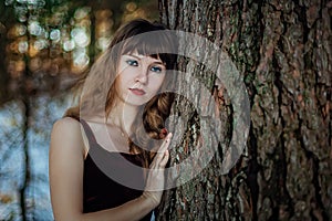 Portrait of a beautiful girl in a dark long dress who stands alone among the trees in the winter forest