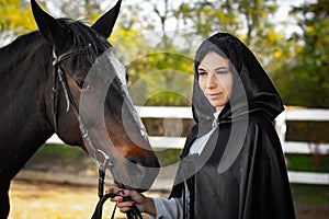 Portrait of a beautiful girl dressed in medieval style, the girl holds a horse by the bridle