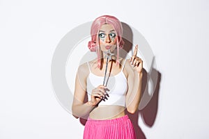 Portrait of beautiful girl in fairy costume looking thoughtful, holding magic wand and wearing pink wig, have an idea