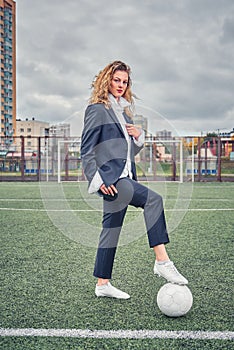 Portrait of  beautiful girl football player in man`s suit on soccer field with ball