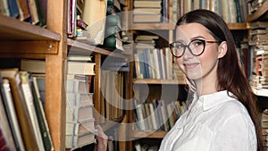 Portrait of a beautiful girl in glasses among the book shelves of the library or archive