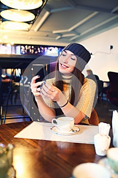 Portrait of beautiful girl in hat using her mobile phone in cafe. Tonned. Selective focus.