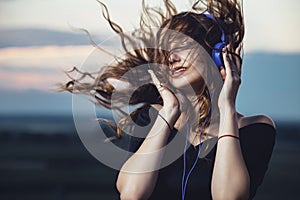 Portrait of a beautiful girl in headphones with flying hair from the wind, young woman listening to music on the nature in the