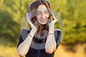 Portrait of a beautiful girl with headphones on head, young woman listening to music on the nature in the field