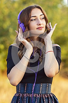 Portrait of a beautiful girl in headphones on head, young woman listening to music on the nature in the field
