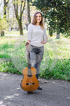 Portrait of a beautiful girl holding her guitar in the park and smiling