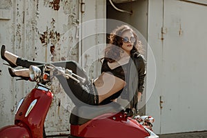 Portrait of a beautiful girl in leather jacket, brassiere and glasses near red motorcycle