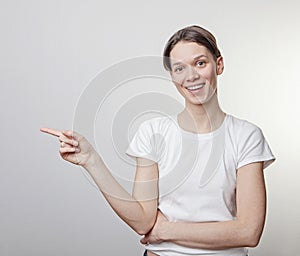 Portrait of beautiful girl, looking at camera and pointing on copy space. Isolated against blank gray studio wall