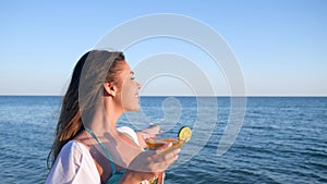 Portrait beautiful girl looks into distance on sea ocean and drink