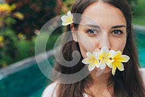 Portrait of beautiful girl with natural make-up and plumeria, frangipani flowers in her mouth