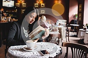 Portrait of a beautiful girl reading book in cafe. drink