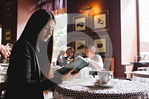 Portrait of a beautiful girl reading book in cafe. drink