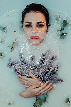Portrait of a beautiful girl with red lipstick and makeup relaxing and resting in the bath with milk and lilac