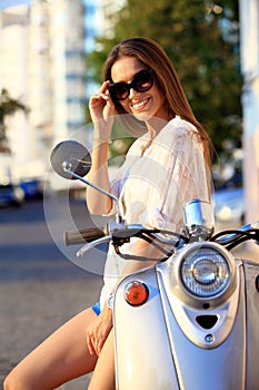 Portrait of a beautiful girl sitting on silver retro scooter, smiling and looking at the camera