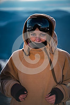 Portrait Beautiful girl at a ski resort against the backdrop of snowy mountains. She is dressed in winter clothes for