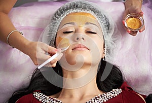 Portrait of beautiful girl applying gold facial mask. Close-up