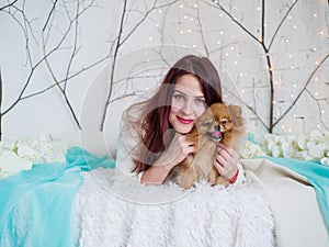 Portrait of a beautiful girl and a spitz dog close-up in a room against the backdrop of garlands