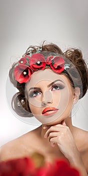 Portrait of beautiful girl in studio with red flowers in her hair and naked shoulders. young woman with professional makeup