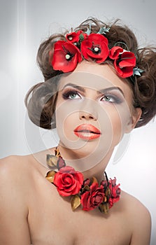 Portrait of beautiful girl in studio with red flowers in her hair and red roses around her neck. Young woman with makeup