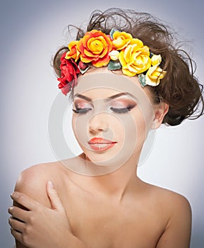 Portrait of beautiful girl in studio with red and yellow roses in her hair and naked shoulders. young woman with makeup