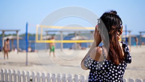 Portrait, beautiful girl in sun glasses wearing big black headphones, listening to music from smartphone, on beach, on