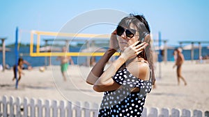 portrait, beautiful girl in sun glasses wearing big black headphones, listening to music from smartphone, on beach, on