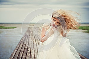 Portrait of a beautiful girl in a wedding dress with her hair flying in the wind on the sea pier