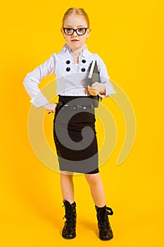 Girl with red hair on a yellow background. A charming girl in transparent glasses holds a pen and a notebook in her