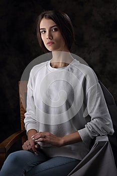 Portrait of a beautiful girl in a white cardigan and blue jeans on a dark background