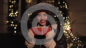 Portrait of Beautiful Girl in Winter Clothes Holding Present Box in her hands, Looking Happy and Smiling, Looking to