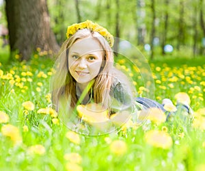 Portrait beautiful girl with a wreath of dandelions lying on the grass