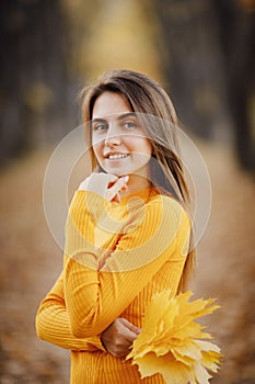 Portrait of beautiful girl in yellow sweater in autumn forest with maple leaves