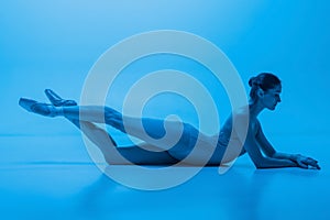 Portrait of beautiful graceful ballet dancer posing isolated on blue studio background in neon light. Art, motion