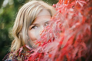 Portrait of beautiful green eyed young woman hiding behind branches of red japanese maple tree