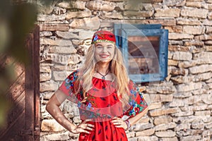 Portrait of beautiful gypsy woman in traditional red dress standing in front of romani camp photo