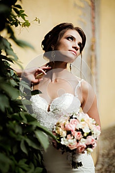 Portrait of a beautiful happy brunette bride in wedding white dress holding hands in bouquet of flowers outdoors