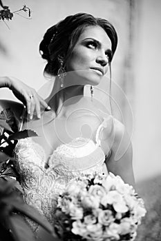 Portrait of a beautiful happy brunette bride in wedding white dress holding hands in bouquet of flowers outdoors