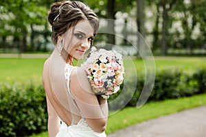 Portrait of a beautiful happy brunette bride in wedding white dress holding hands in bouquet of flowers outdoors