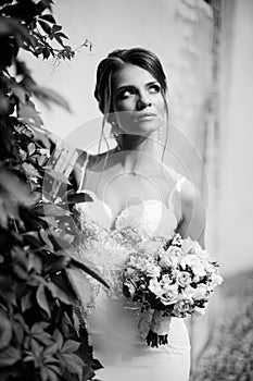 Portrait of a beautiful happy brunette bride in wedding white dress holding hands in bouquet of flowers outdoors