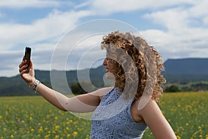 Portrait of beautiful happy Caucasian girl making selfie photo on smartphone while standing in golden field.