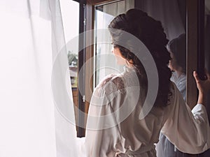 Portrait of beautiful happy cheerful brunette woman in white silk robe standing by the window