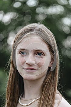 Portrait of a beautiful happy girl with blond hair and freckles looking at the camera and smiling charmingly, closeup, outdoors