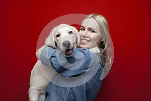 Portrait of a beautiful happy girl with a dog on a red background, a woman holds a golden retriever puppy and smiles