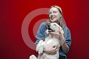 Portrait of a beautiful happy girl with a dog on a red background, a woman holds a golden retriever puppy and smiles