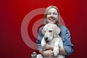 Portrait of a beautiful happy girl with a dog on a red background, a woman holds a golden retriever puppy and smiles