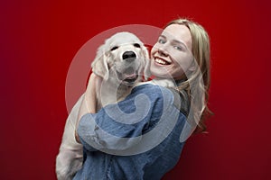 Portrait of a beautiful happy girl with a dog on a red background, a woman holds a golden retriever puppy and smiles