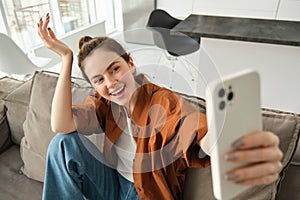 Portrait of beautiful happy girl takes selfies on sofa. Woman posing for photos on her couch, taking pictures for social