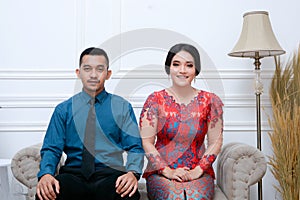 Portrait of beautiful happy indonesian couple wearing traditional costume sitting on couch.