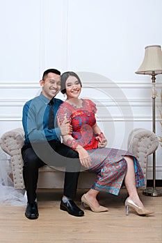 Portrait of beautiful happy indonesian couple wearing traditional costume sitting on couch
