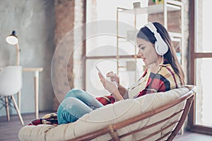 Portrait of beautiful happy latin girl sitting in stylish armchair at home with phone and listen to music with white